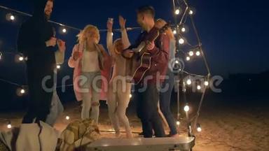 <strong>海滩</strong>派对，快乐的男人和女孩与吉他音乐舞蹈和笑声在花环照明